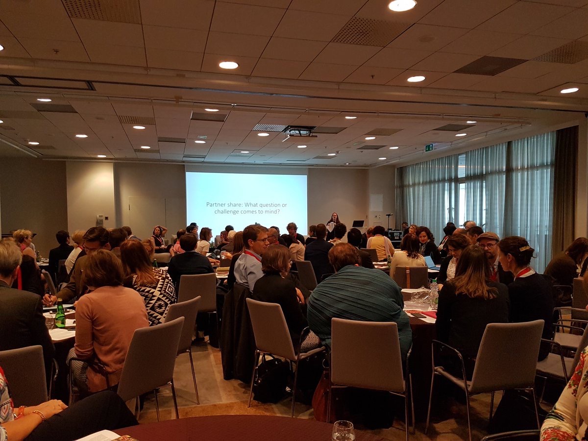 Several round tables full of people talking with one another.