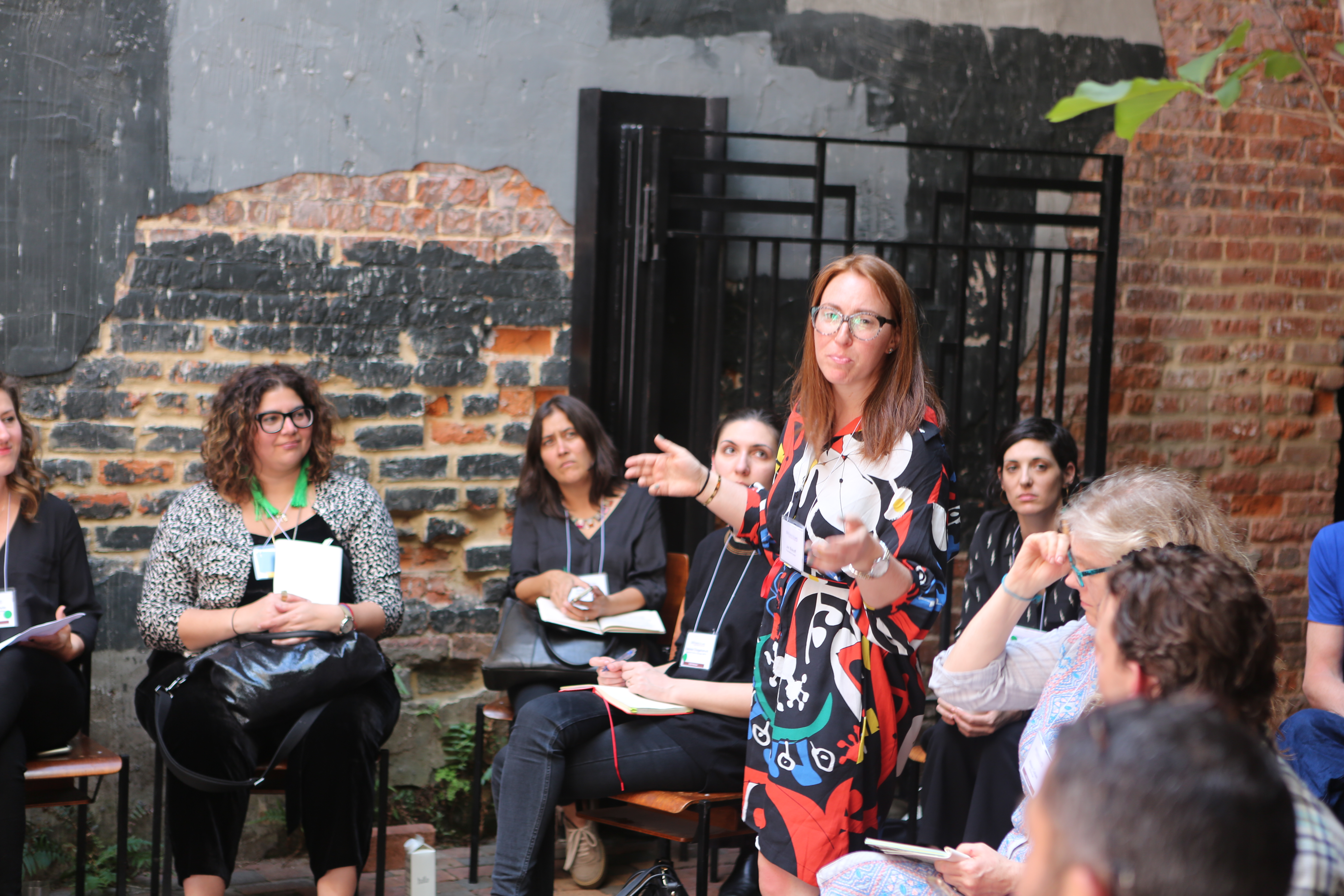 A girl in a multicolored dress stands with arms open in the middle of a circle of other people.